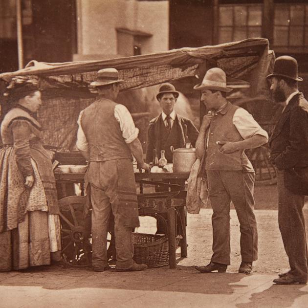 Londoners gather around a seller of shellfish. The four men pictured sport a variety of hat shapes and sizes. (SWNS)